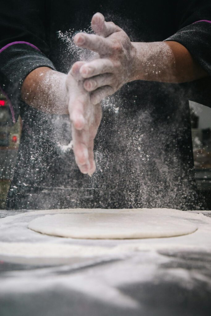 pexels photo 784633 784633 A chef clapping hands over dough, releasing flour in a kitchen setting.